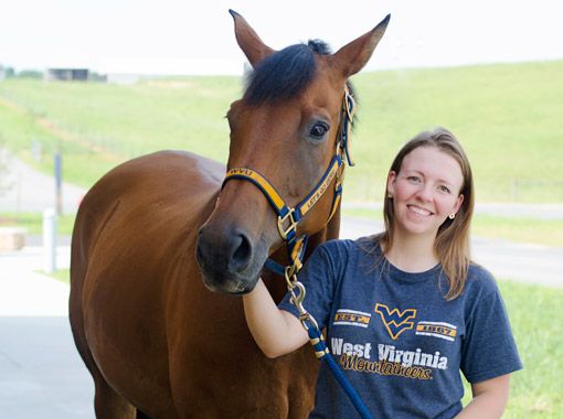 
                Student in WVU t-shirt posing with a horse at the farm
            