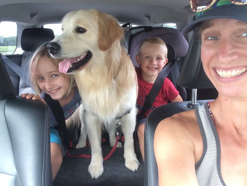 Photo of a woman, little girl and little boy in car with golden retriever dog.
