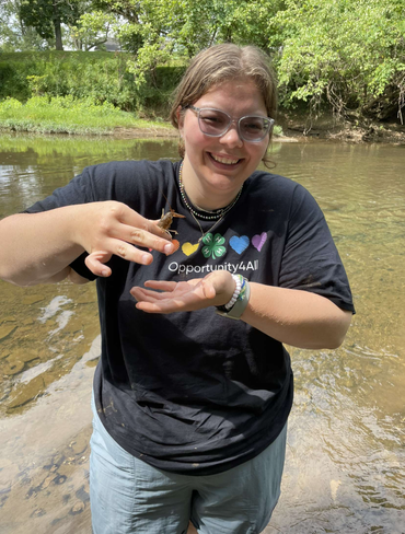 Photo of young woman at a stream holding a bug.